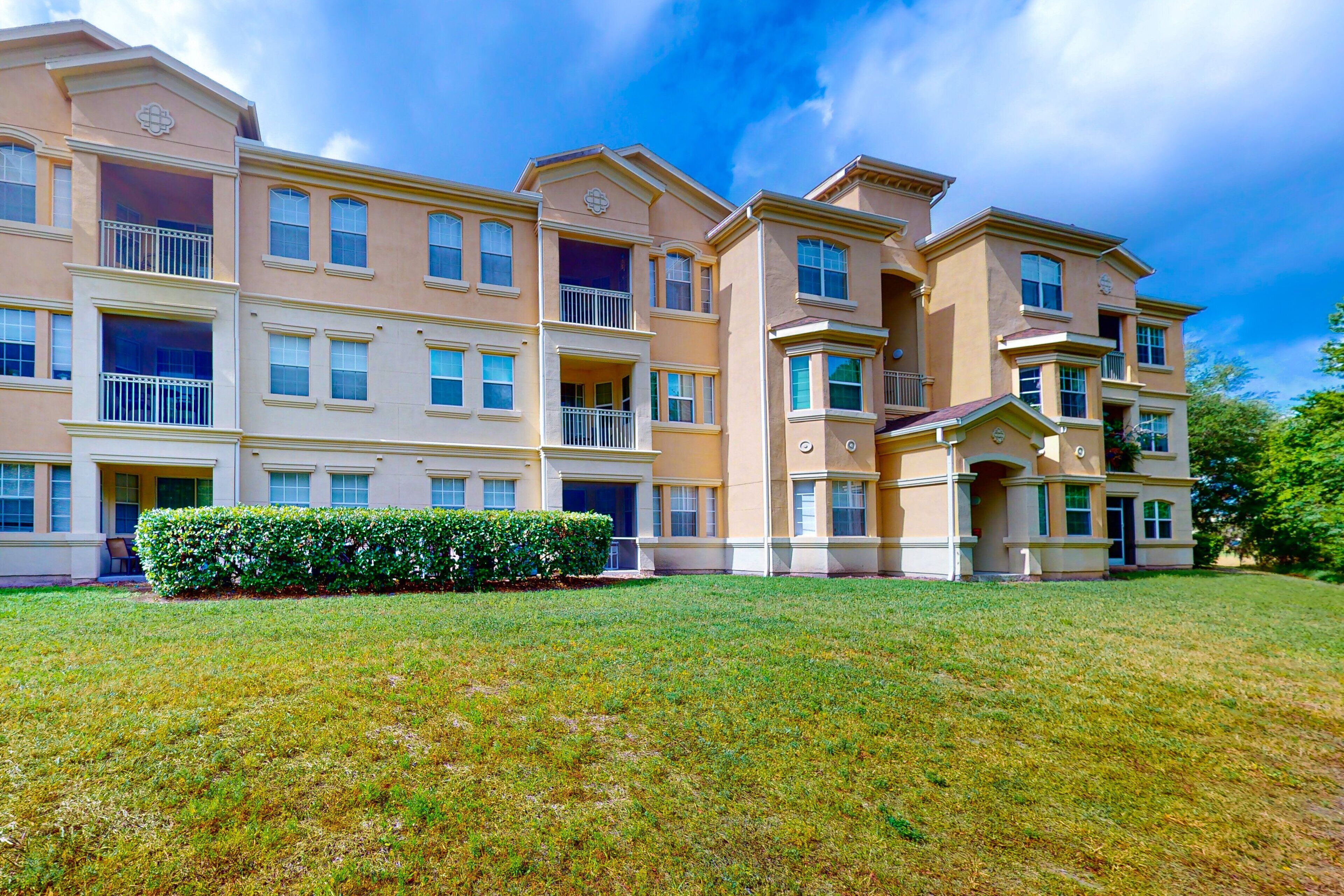 A multi-story residential building with balconies, a well-maintained lawn, and a clear sky.