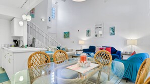 A modern kitchen with white cabinets, a dining area with a glass table, wicker chairs, and a blue sofa. - Breezy Townhouse With a Pool, hot Tub, Patio, Central AC, and Washer/dryer (Kissimmee)