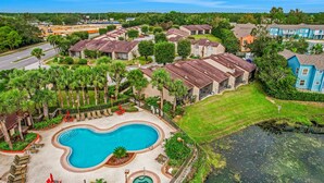 A residential area with a swimming pool, houses, and a small body of water. - Breezy Townhouse With a Pool, hot Tub, Patio, Central AC, and Washer/dryer (Kissimmee)