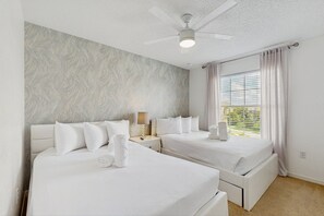 Une chambre d’hôtel avec deux lits, un ventilateur de plafond, une fenêtre avec des rideaux et un mur au motif texturé.