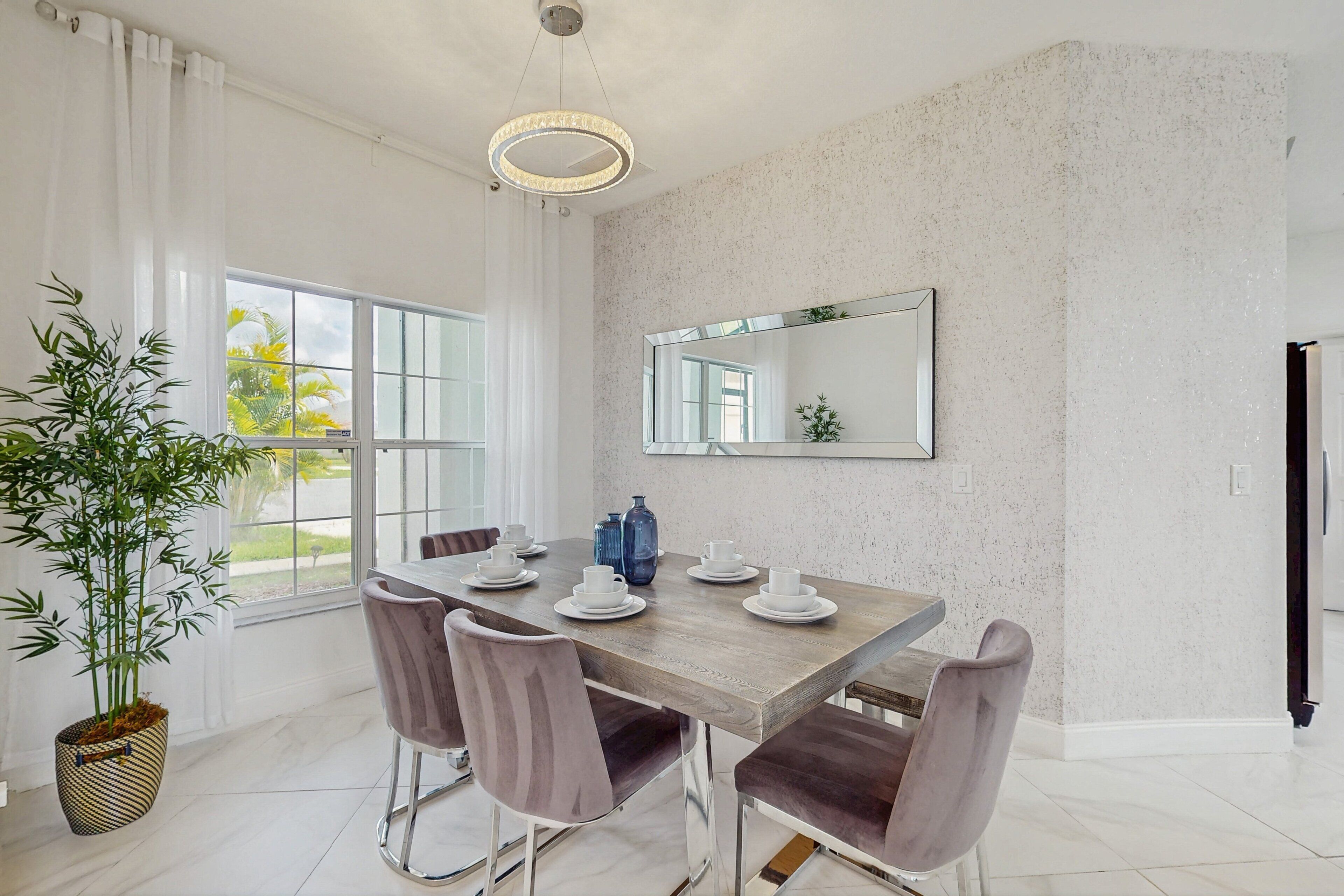 A dining area with a wooden table, four chairs, a large mirror, and a potted plant.