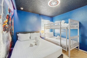 Une chambre avec deux lits, un lit superposé, une affiche et un luminaire au plafond.