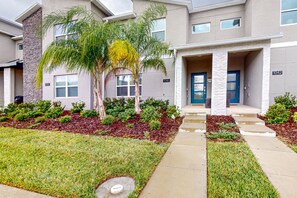 A modern building with numbered doors, a well-maintained lawn, and a small palm tree. - Beautiful Sun-inspired Home in Champions Gate Community With Resort Amenities (Davenport)