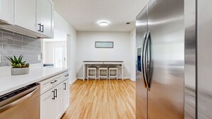 Una cucina con mobili bianchi, un frigorifero in acciaio inossidabile, un pavimento in legno e un cartello con la scritta 'Home'.
