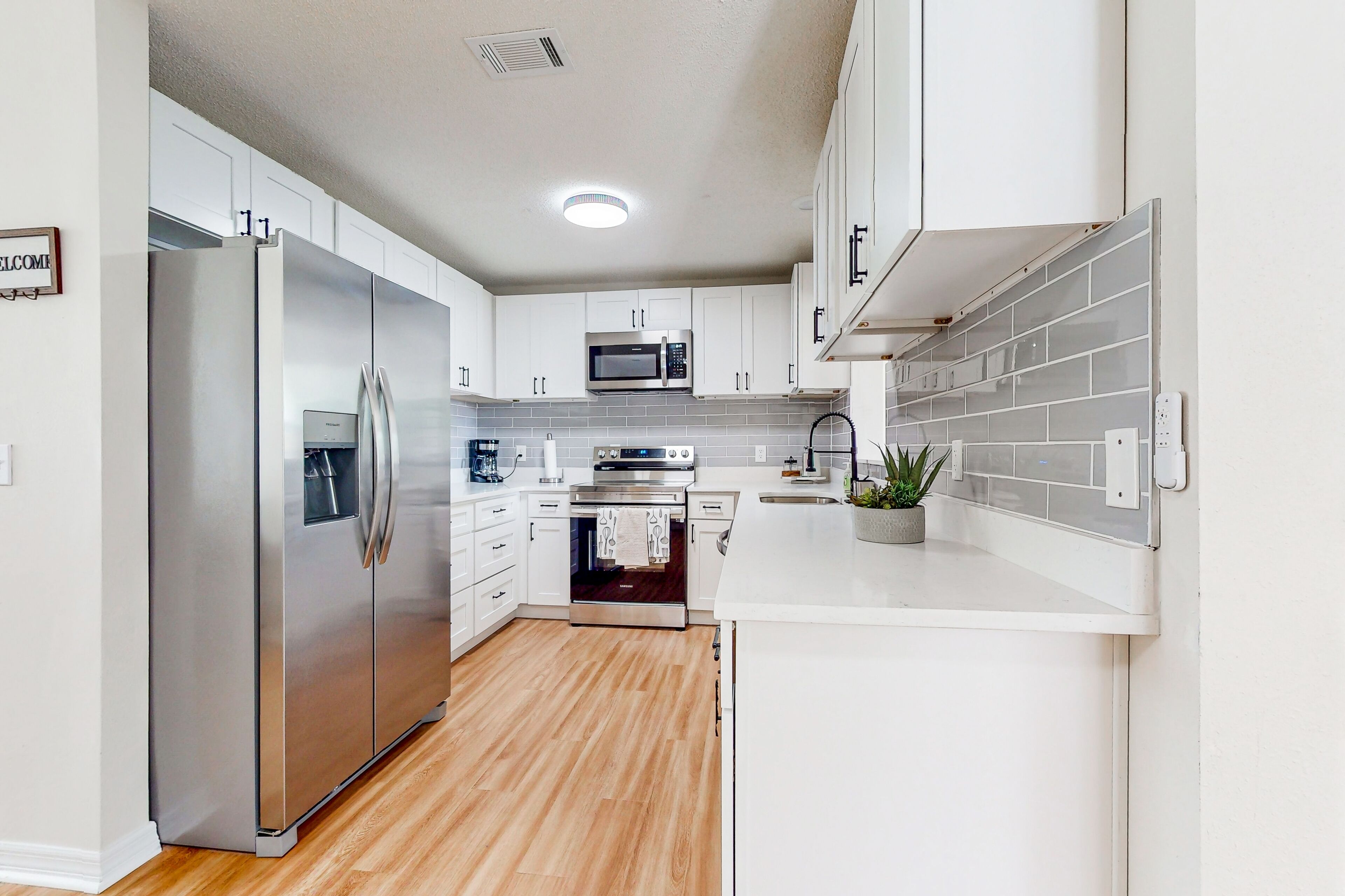 A modern kitchen with white cabinets, stainless steel appliances, and a wooden floor.