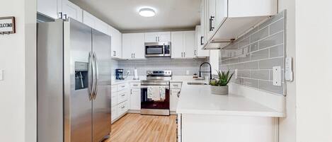 A modern kitchen with white cabinets, stainless steel appliances, and a wooden floor.