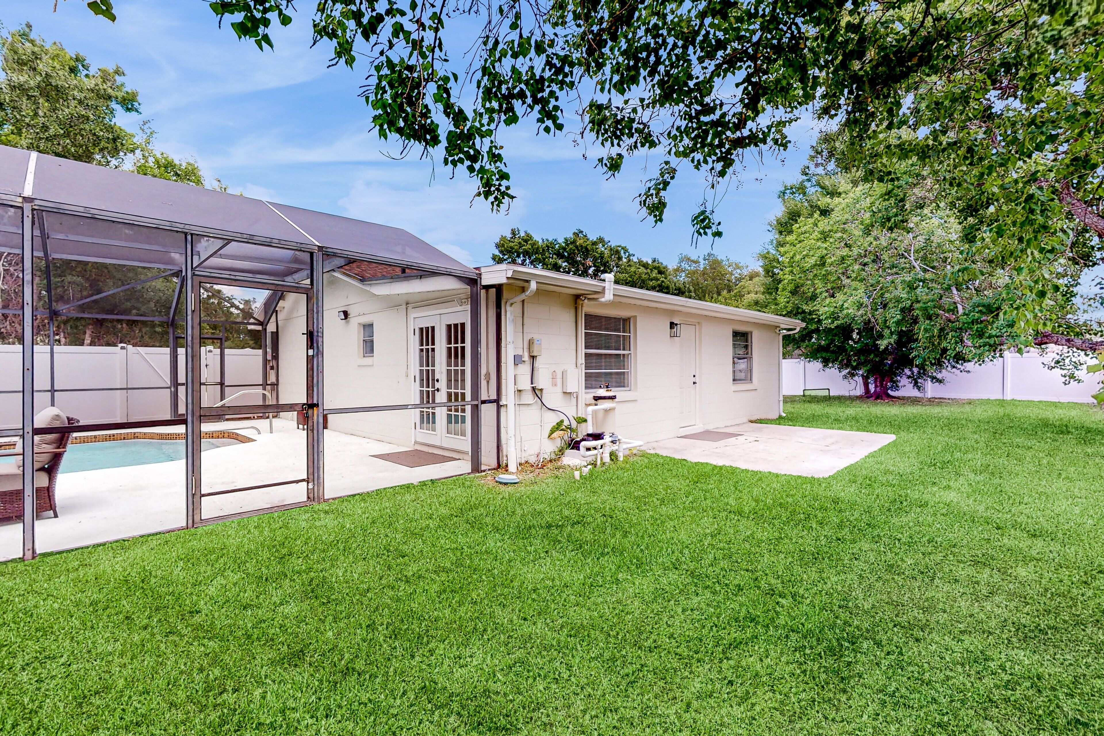 Una casa con un patio cubierto, piscina y césped cuidado.