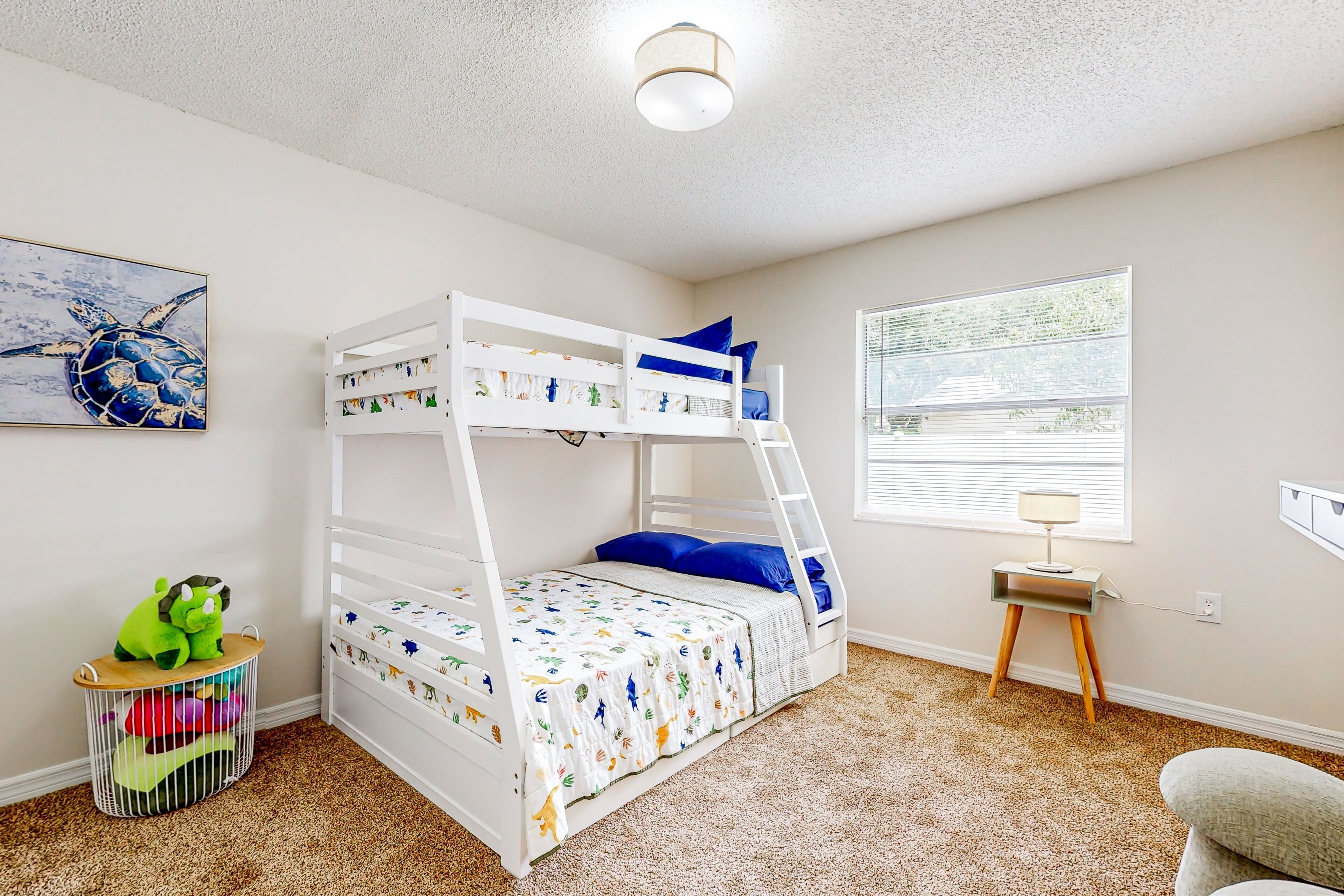 A bunk bed with a white frame, a small bedside table with a lamp, and a window with blinds.