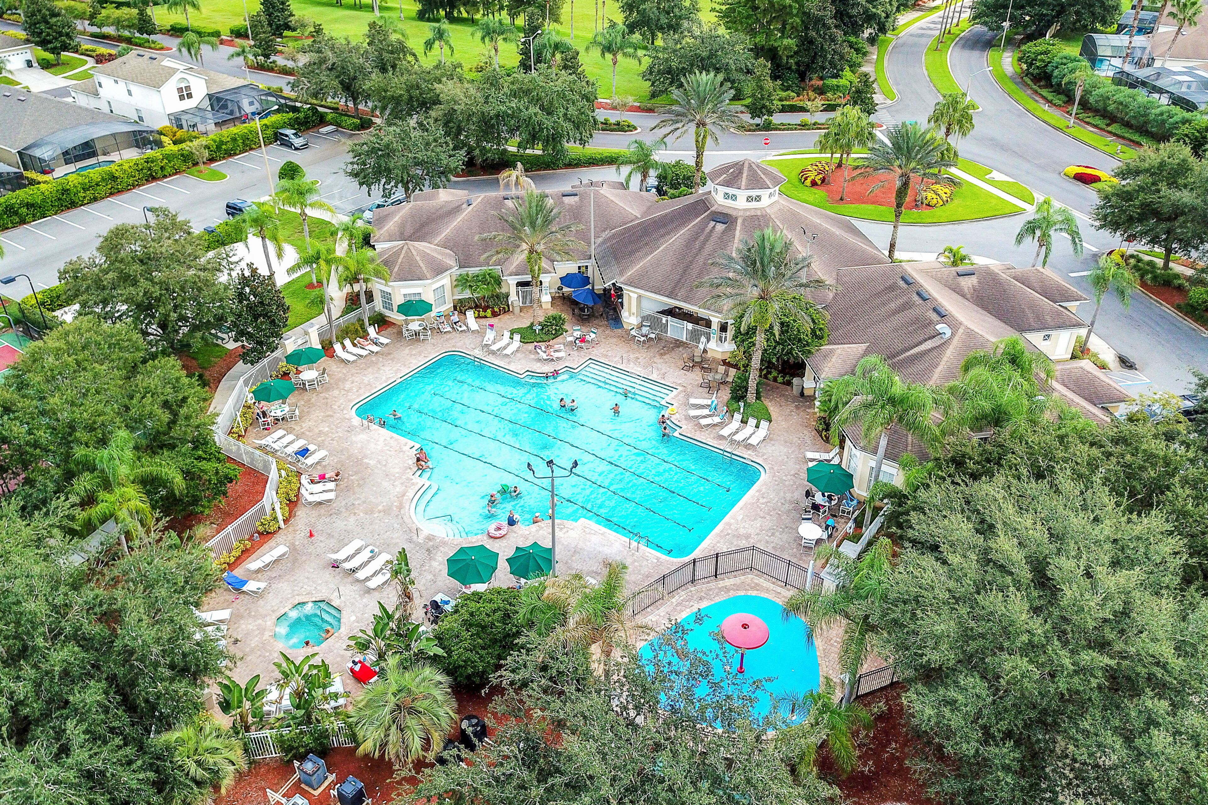 A large swimming pool with multiple lanes, surrounded by lounge chairs and umbrellas, and adjacent to a building with a tiled roof.