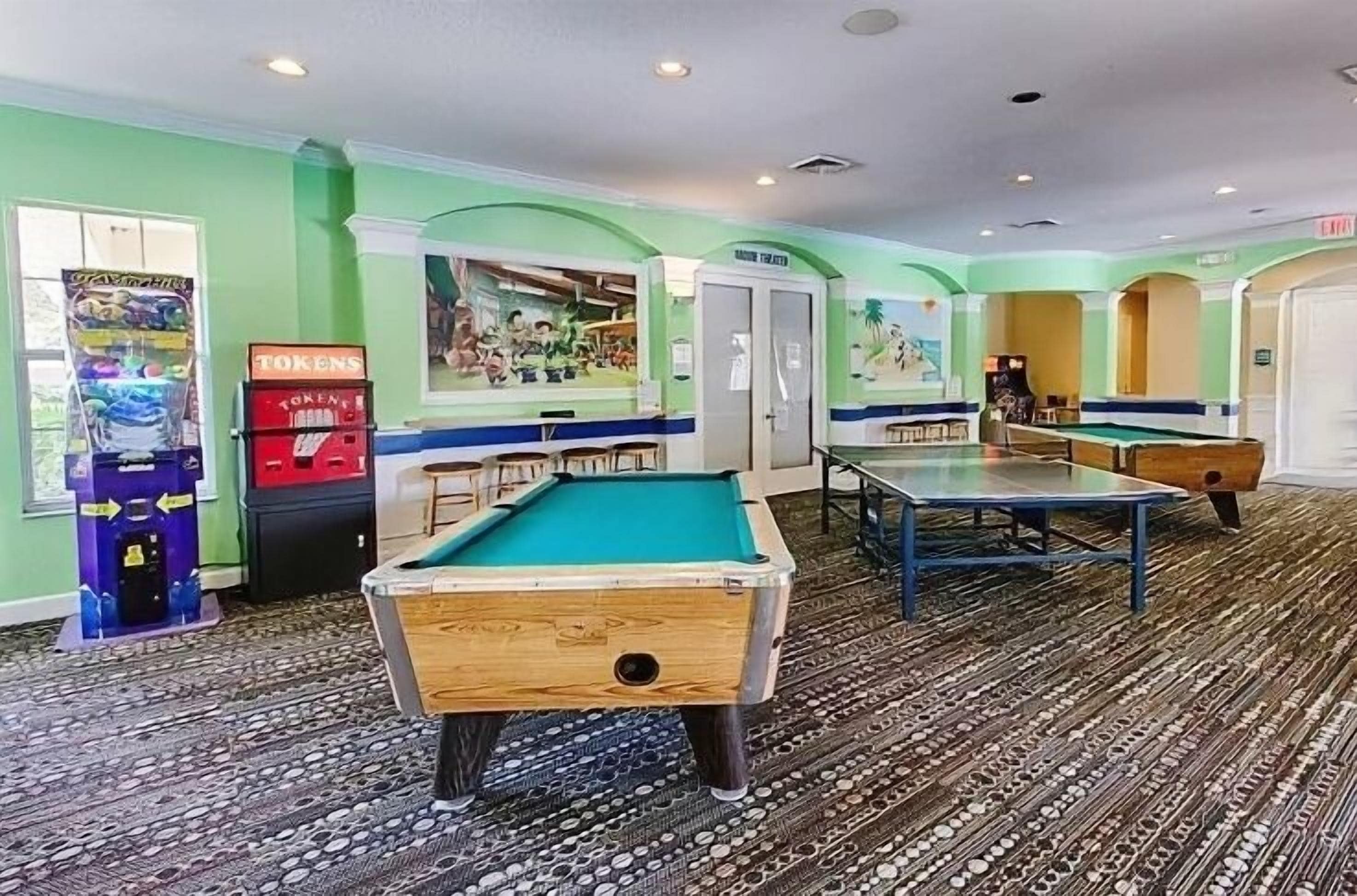 A pool table, a dartboard, and a jukebox in a room with green walls and patterned carpet.