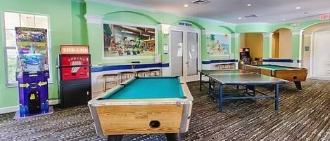 A pool table, a dartboard, and a jukebox in a room with green walls and patterned carpet.