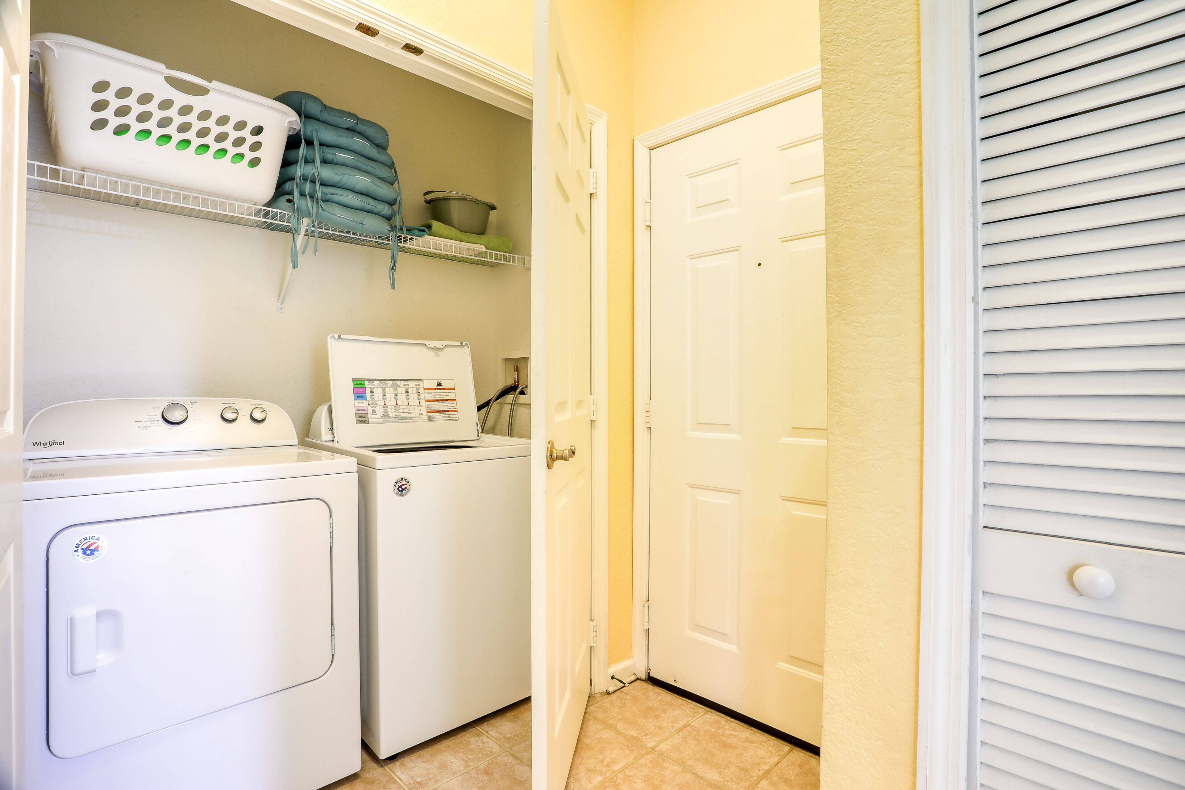 A laundry room with a front-loading washer and dryer, shelves with laundry baskets and folded clothes, and a white door.