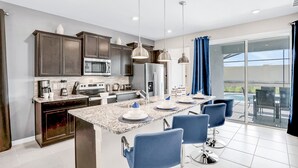 A modern kitchen with granite countertops, dark cabinetry, stainless steel appliances, and a dining area with blue chairs. - Spacious Resort Home With Private Pool, Game Room, & Abundant Amenities (Davenport)