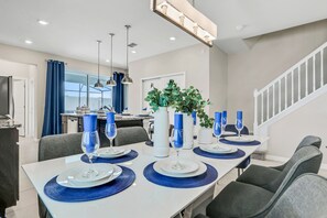 A dining area with a long table set for six, blue placemats, white plates, and blue glassware. - Spacious Resort Home With Private Pool, Game Room, & Abundant Amenities (Davenport)