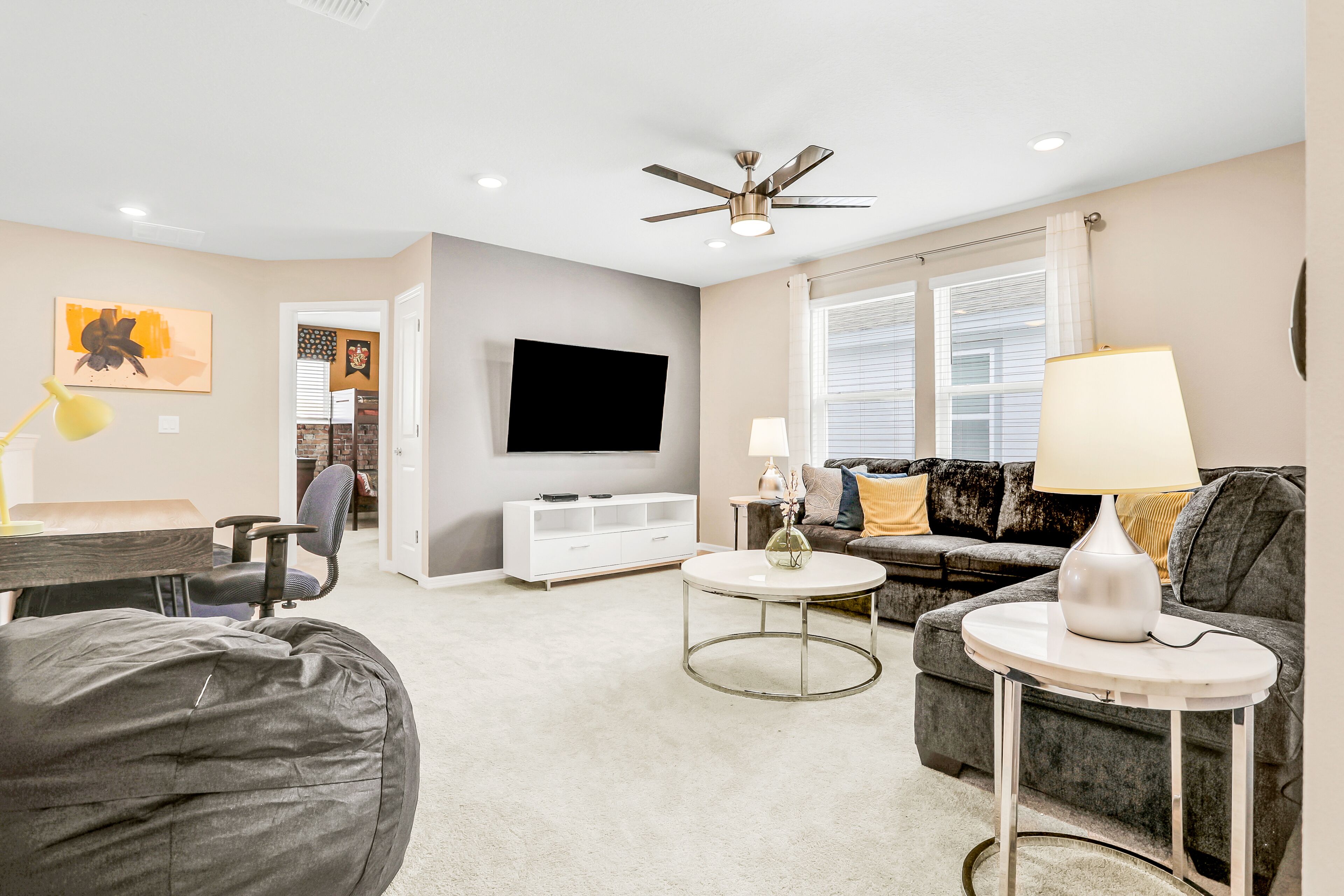 A modern living room with a flat-screen TV, a ceiling fan, a sofa, a coffee table, and a lamp.