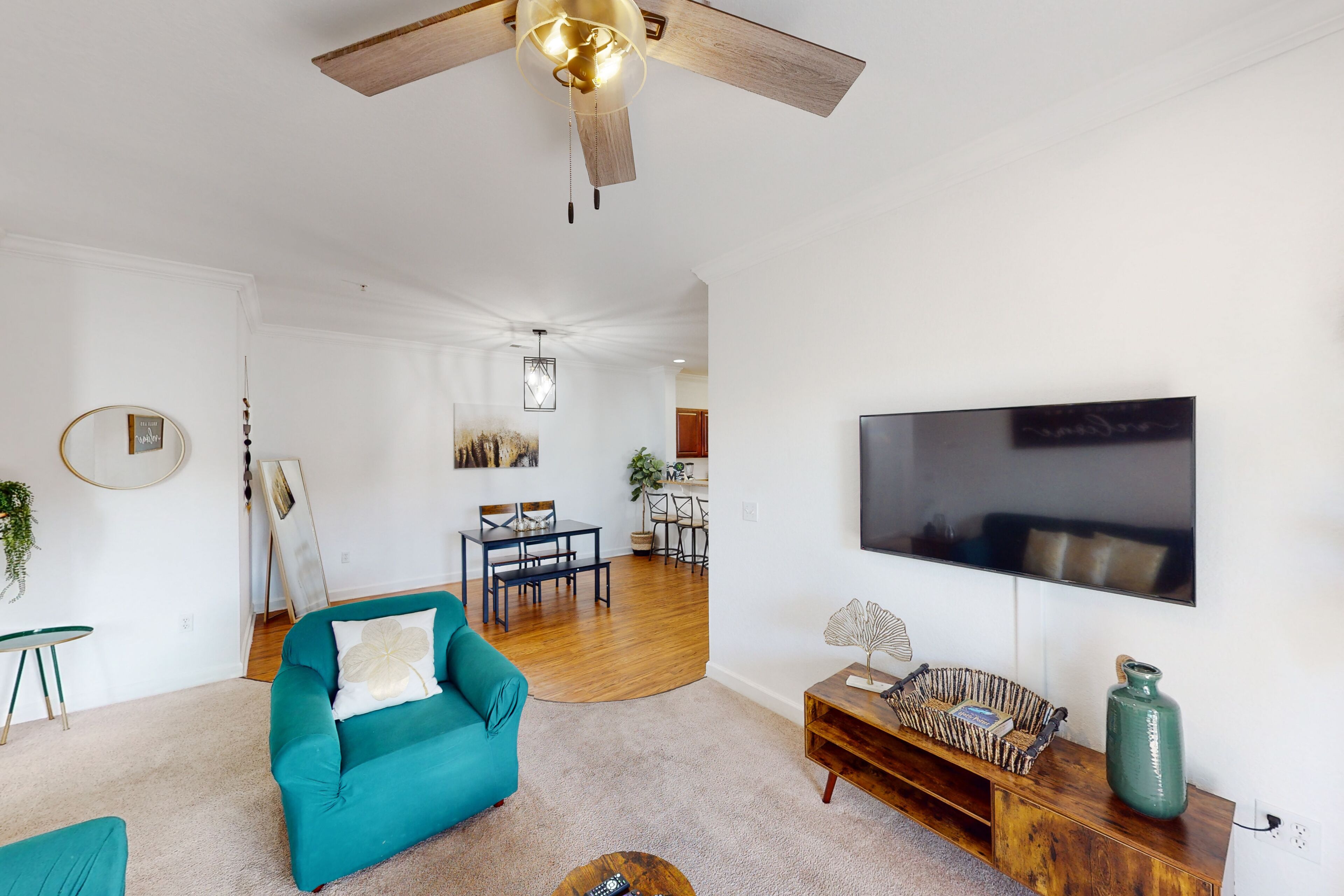 A spacious living room with a teal sofa, wooden coffee table, and a TV mounted on the wall.