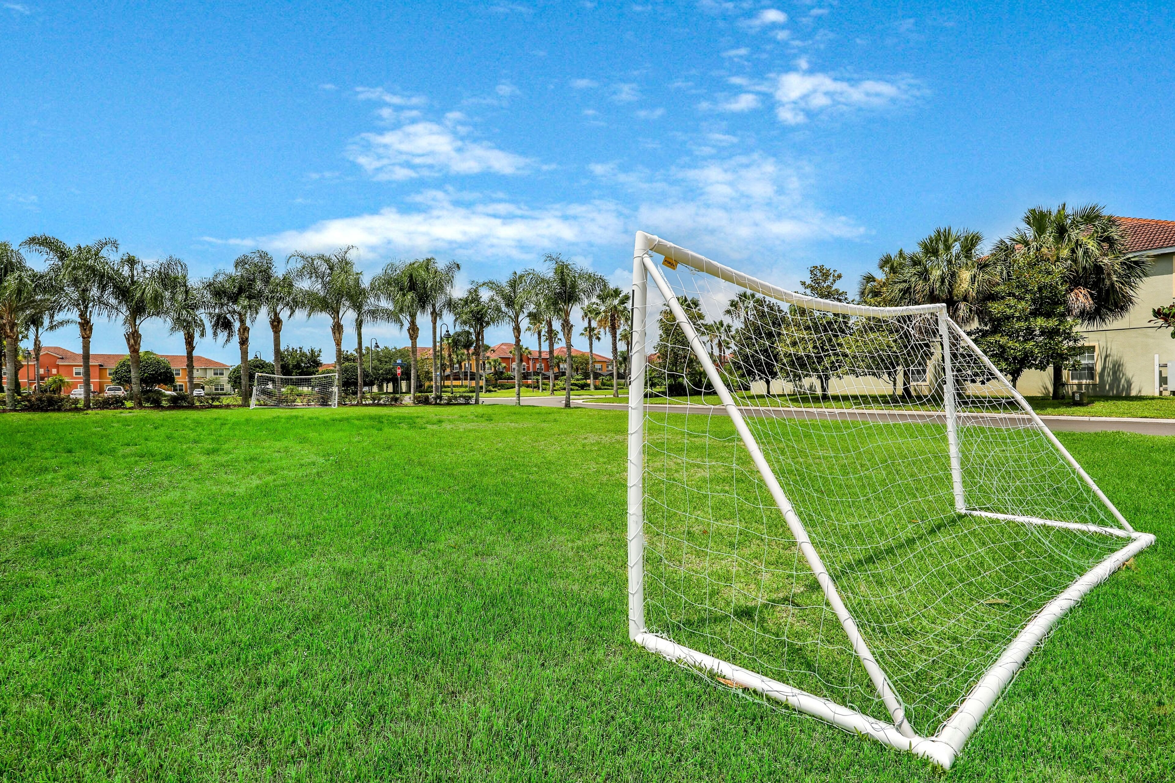 A soccer goal on a well-maintained grassy field with a clear sky and palm trees in the background.