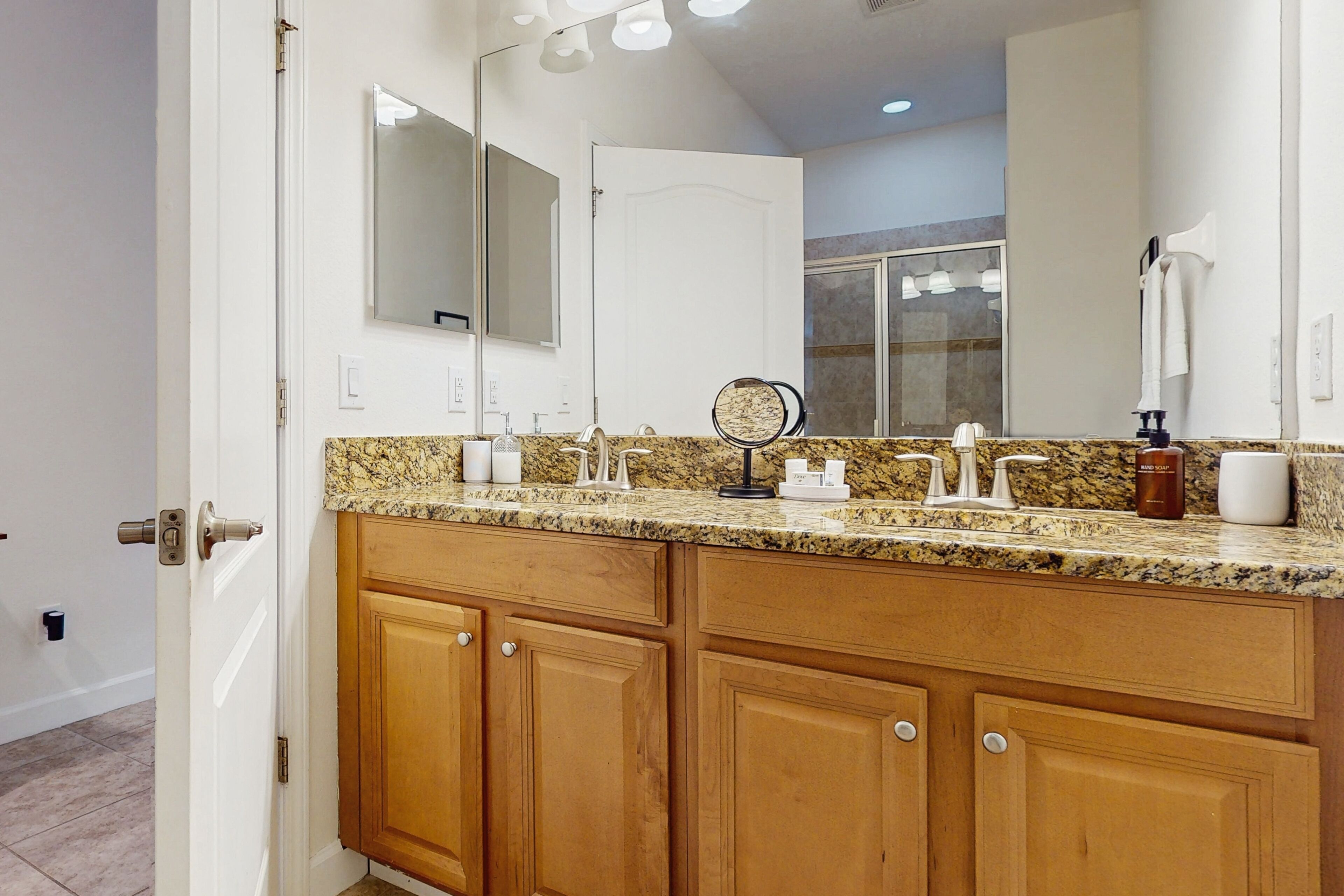 A bathroom with a granite countertop, wooden cabinets, a large mirror, and a towel rack.