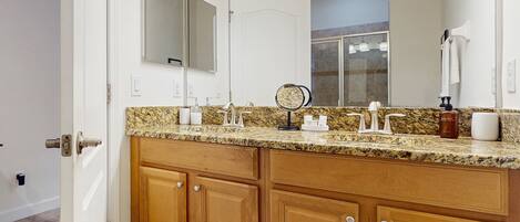 A bathroom with a granite countertop, wooden cabinets, a large mirror, and a towel rack.