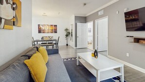 A modern living room with a sofa, a dining table, and a TV mounted on the wall. - Tuscan Lane (Davenport)