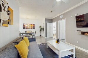 Ein modernes Wohnzimmer mit einer Couch, einem Esstisch und einem an der Wand befestigten Fernseher.