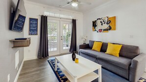 A living room with a gray sofa, yellow pillows, a white coffee table, a ceiling fan, and a large window with curtains. - Tuscan Lane (Davenport)
