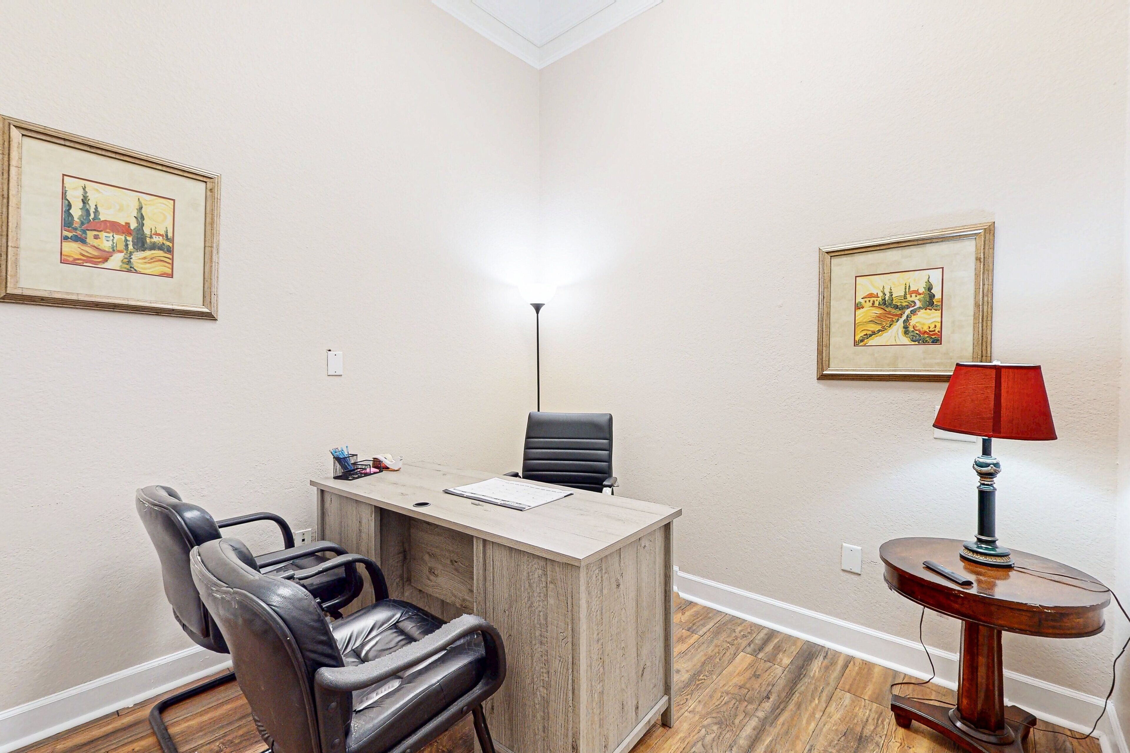 Une pièce comprenant un bureau, deux chaises, une lampe et deux tableaux encadrés accrochés aux murs.