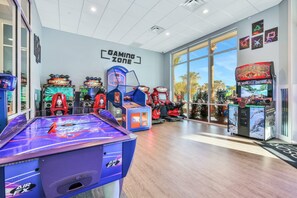 Un espace de jeux comprenant divers jeux d’arcade, notamment des jeux de hockey sur air et des jeux de course, dans un espace intérieur bien éclairé et doté de grandes fenêtres.