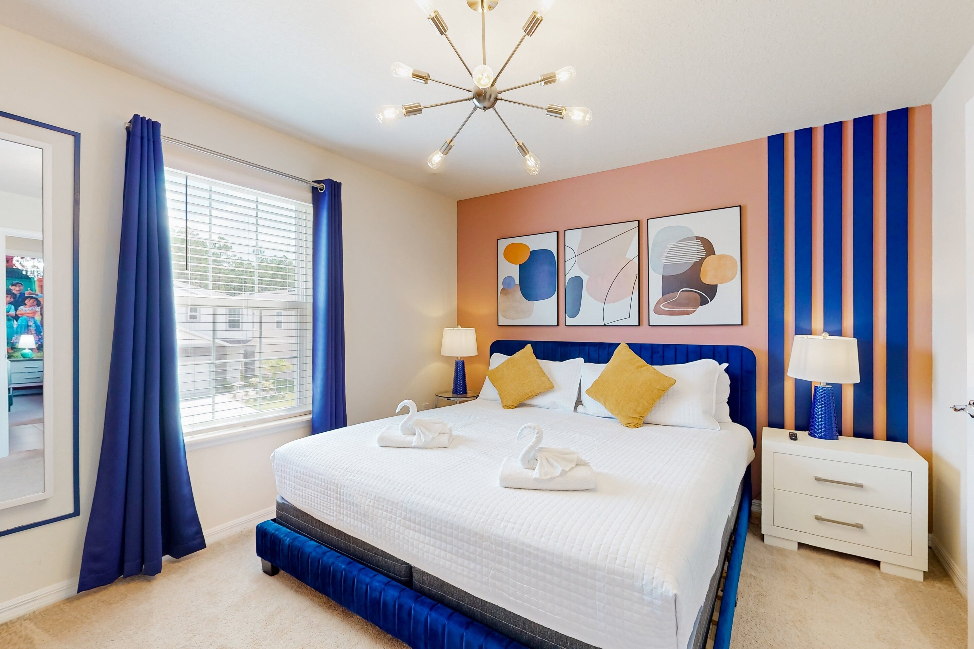 A hotel room with a bed, a nightstand, a lamp, a window with curtains, and wall art.