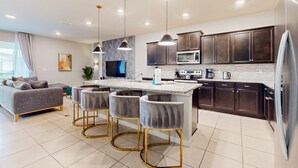 A modern kitchen with dark cabinets, a central island, bar stools, and pendant lighting. - Inviting Family-friendly Home W/private Pool, Spa, Central AC, & W/D (Davenport)