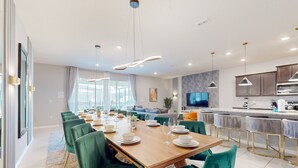 A modern dining area with a wooden table set for six, green upholstered chairs, and pendant lighting. - Inviting Family-friendly Home W/private Pool, Spa, Central AC, & W/D (Davenport)