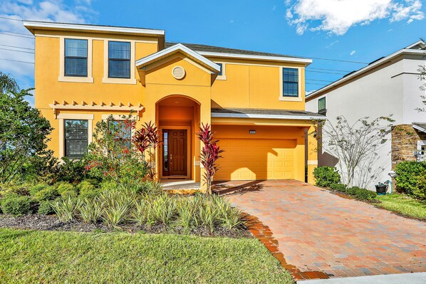 A two-story house with a yellow facade, a front entrance, and a brick driveway. - Modern Family Home - Private Pool, Lanai, Wifi, Central AC & Washer-dryer (Davenport)