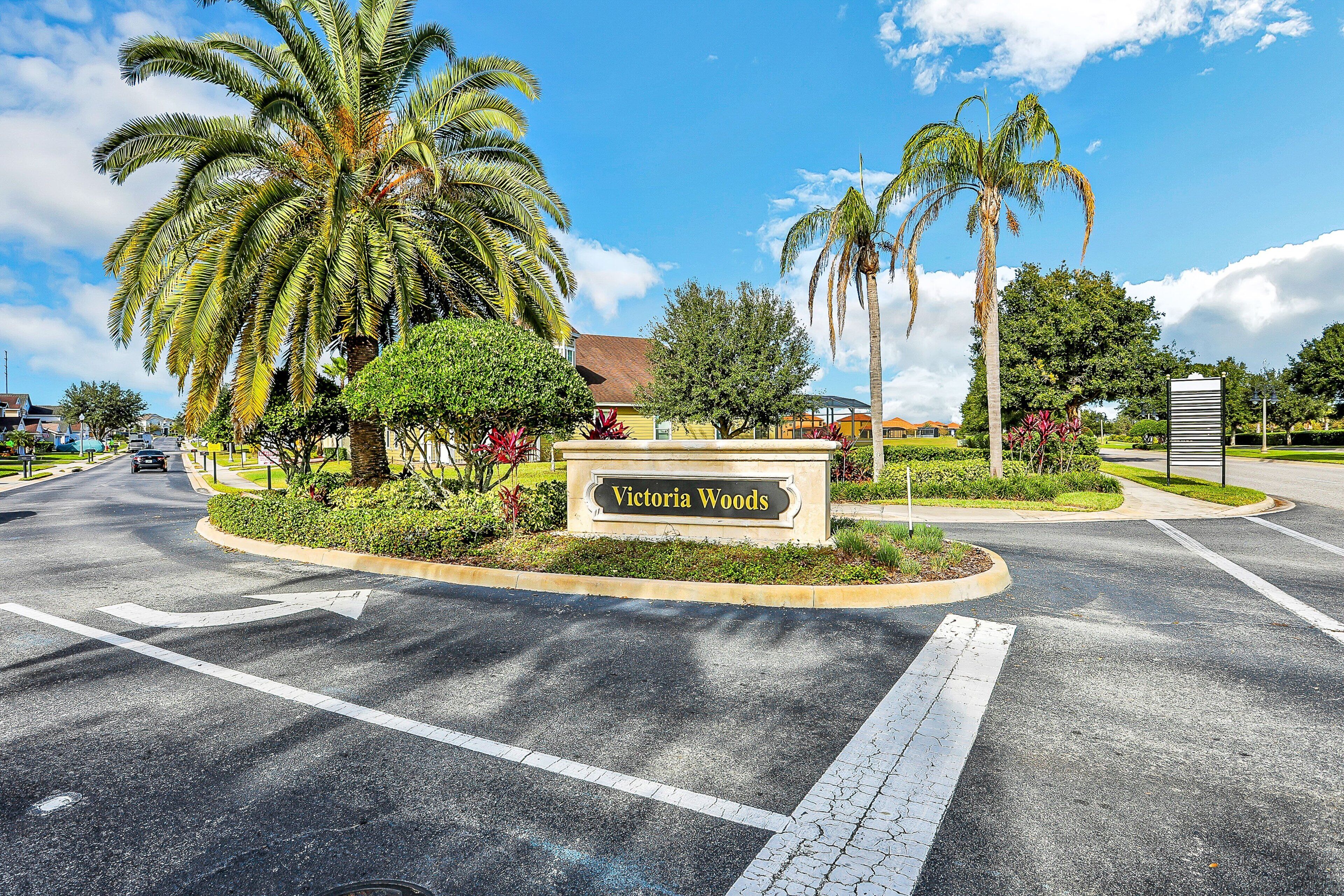 A street sign for 'Victoria Woods' with a road layout including a pedestrian crossing and palm trees.