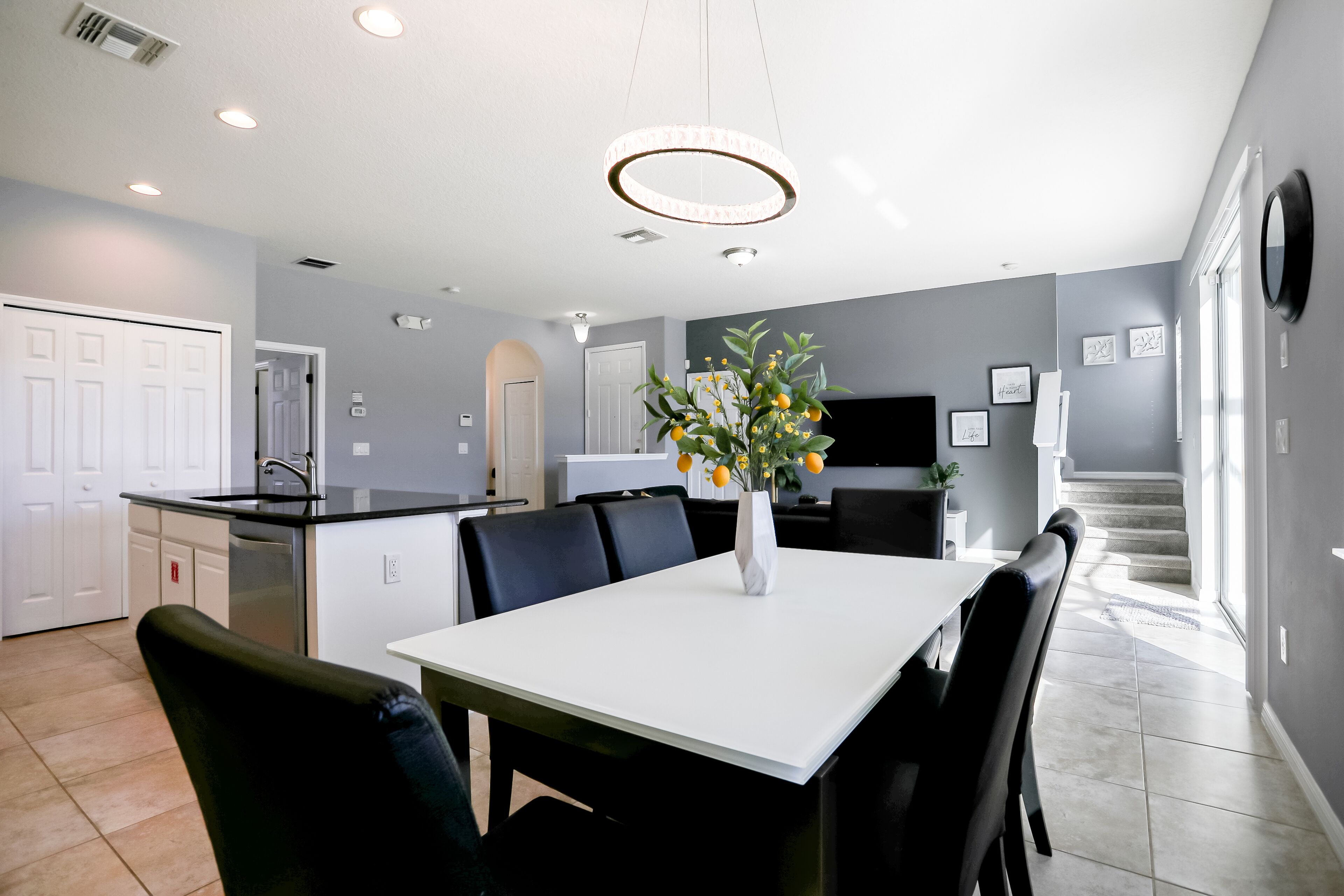 A modern kitchen with a white countertop, black chairs, and a vase with flowers.