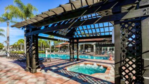 Ein Poolbereich mit Pergola, Liegestühlen und gefliestem Boden.
