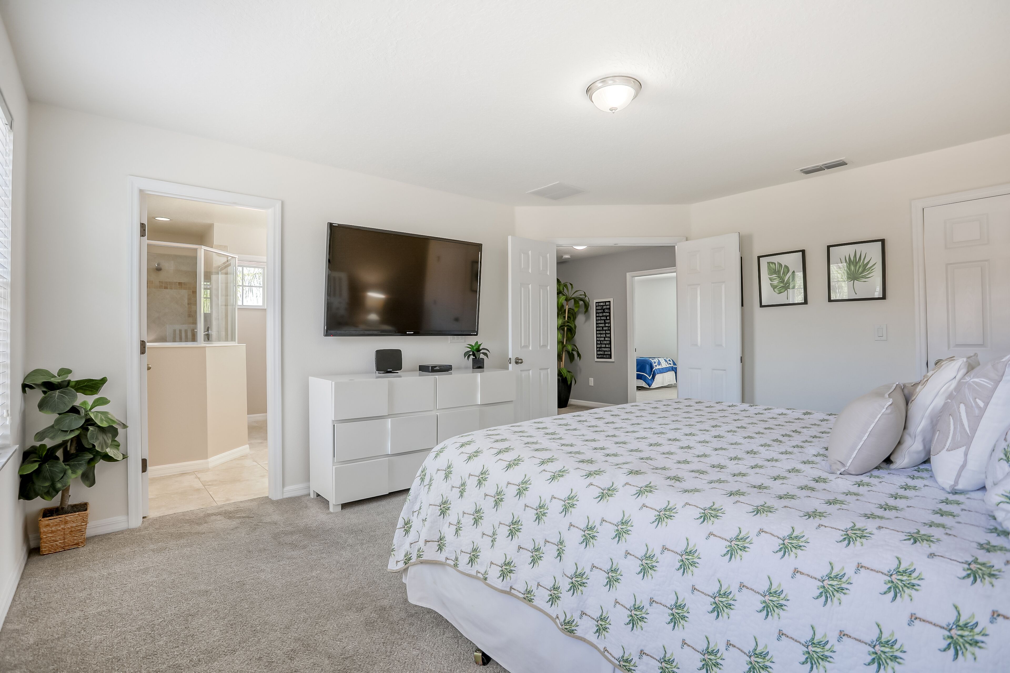 A bedroom with a bed, a TV, a white dresser, and a door leading to a bathroom.