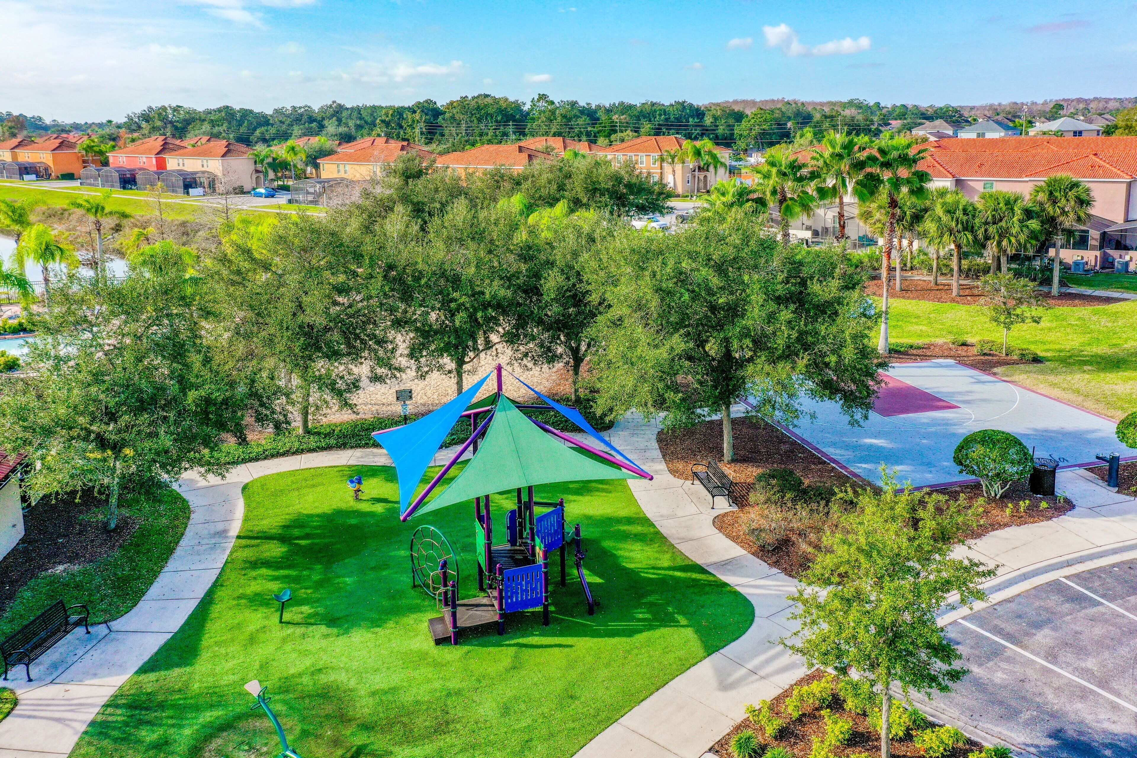A playground with a green and purple canopy, surrounded by a well-maintained lawn and trees.