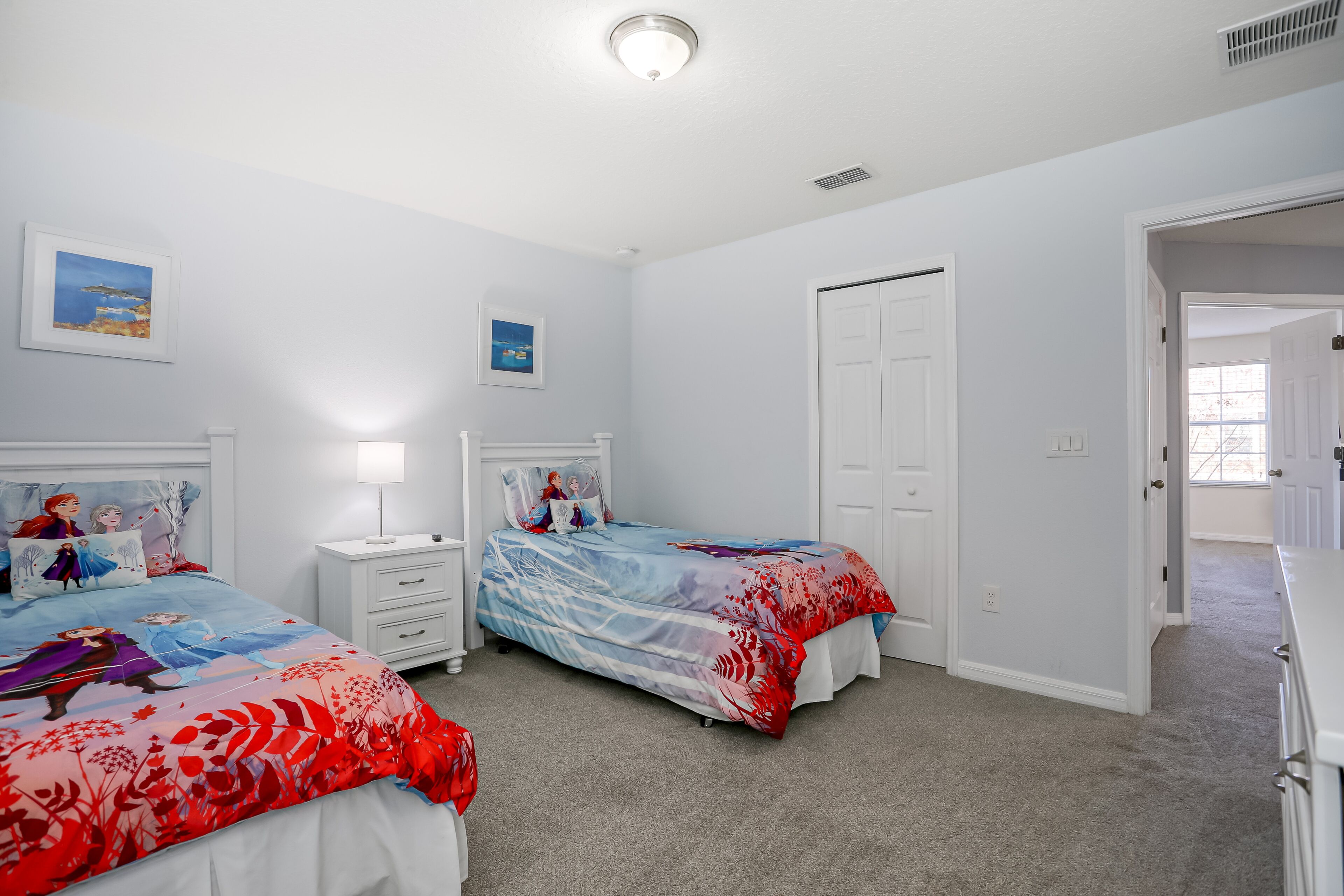 A bedroom with two beds, white walls, and a door leading to another room.