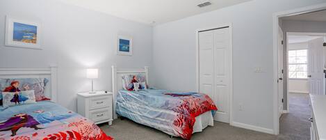A bedroom with two beds, white walls, and a door leading to another room.