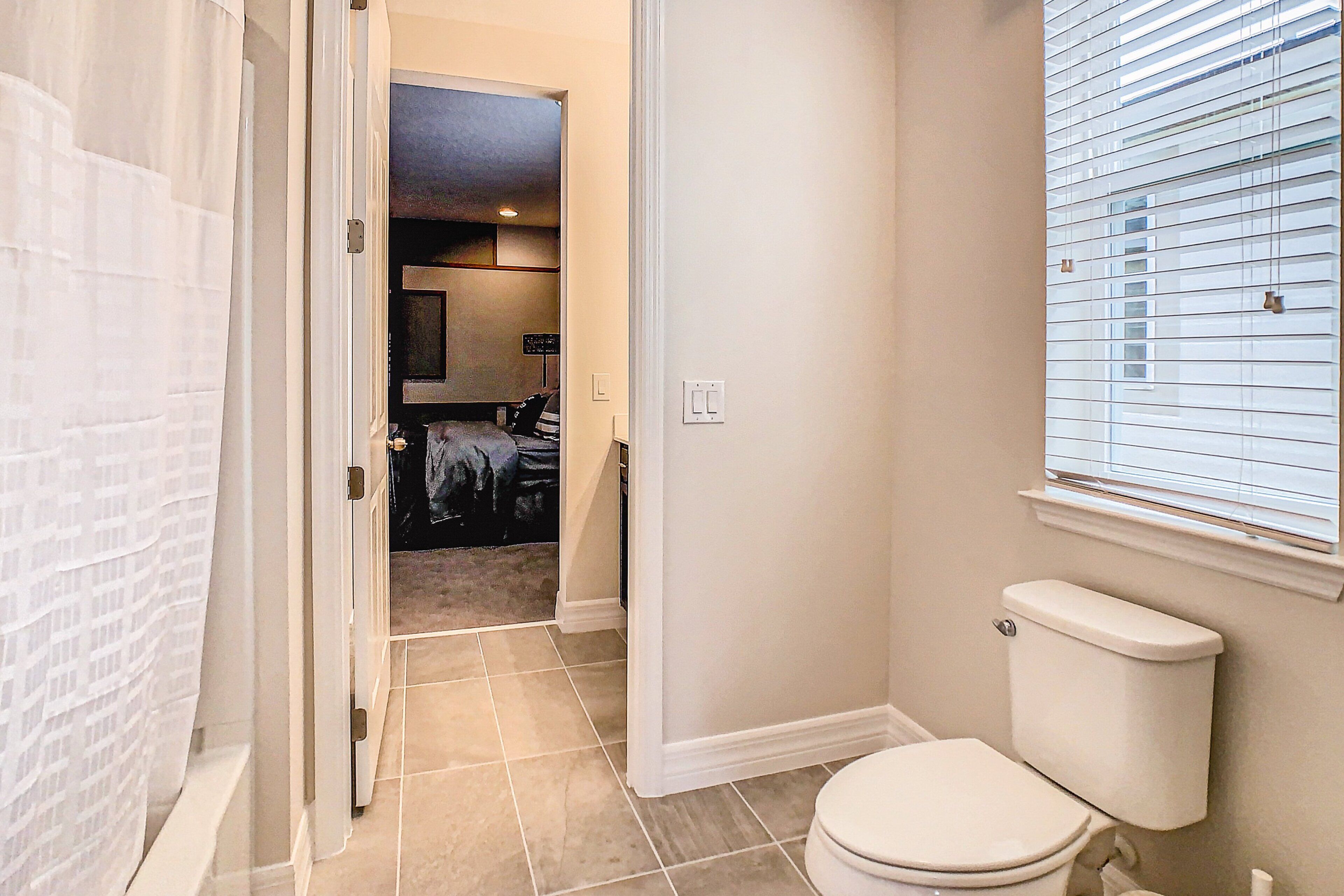 Une salle de bain avec des toilettes, un rideau de douche et une fenêtre avec des stores.