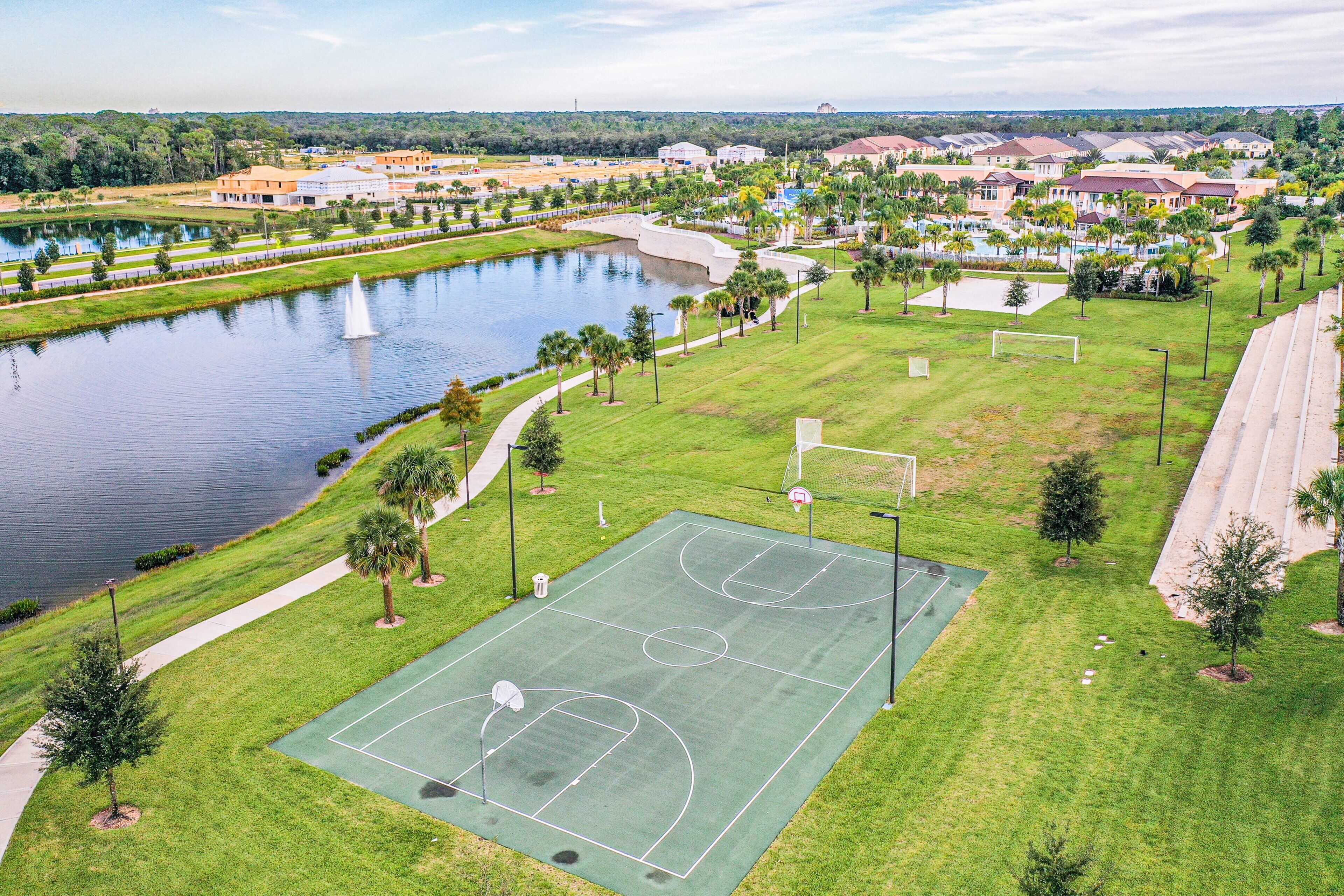 Un terrain de basket entouré d’un parc comprenant un lac, des arbres et des immeubles d’habitation.