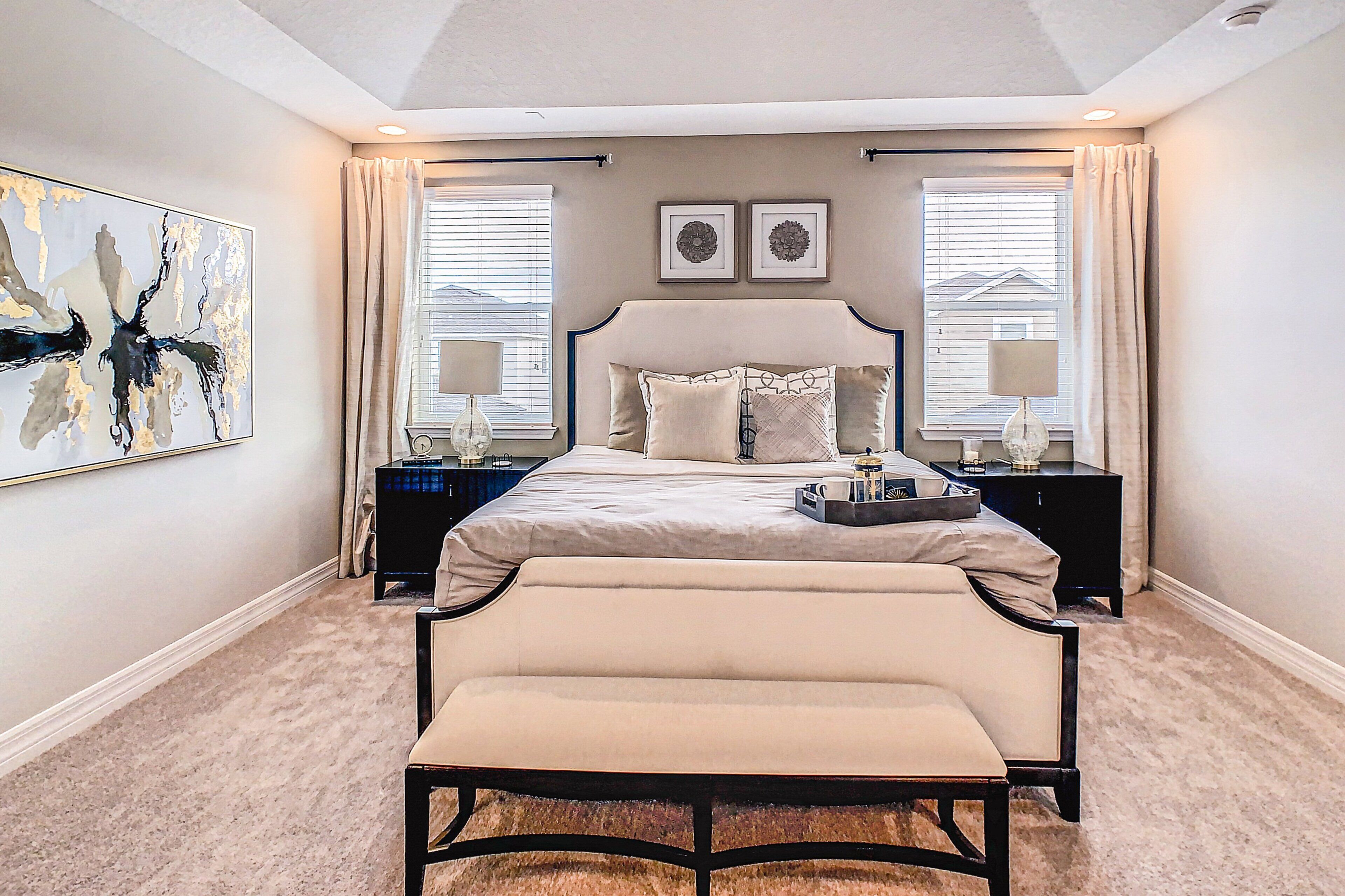 A bedroom with a bed, bedside tables, a bench, and artwork on the walls.