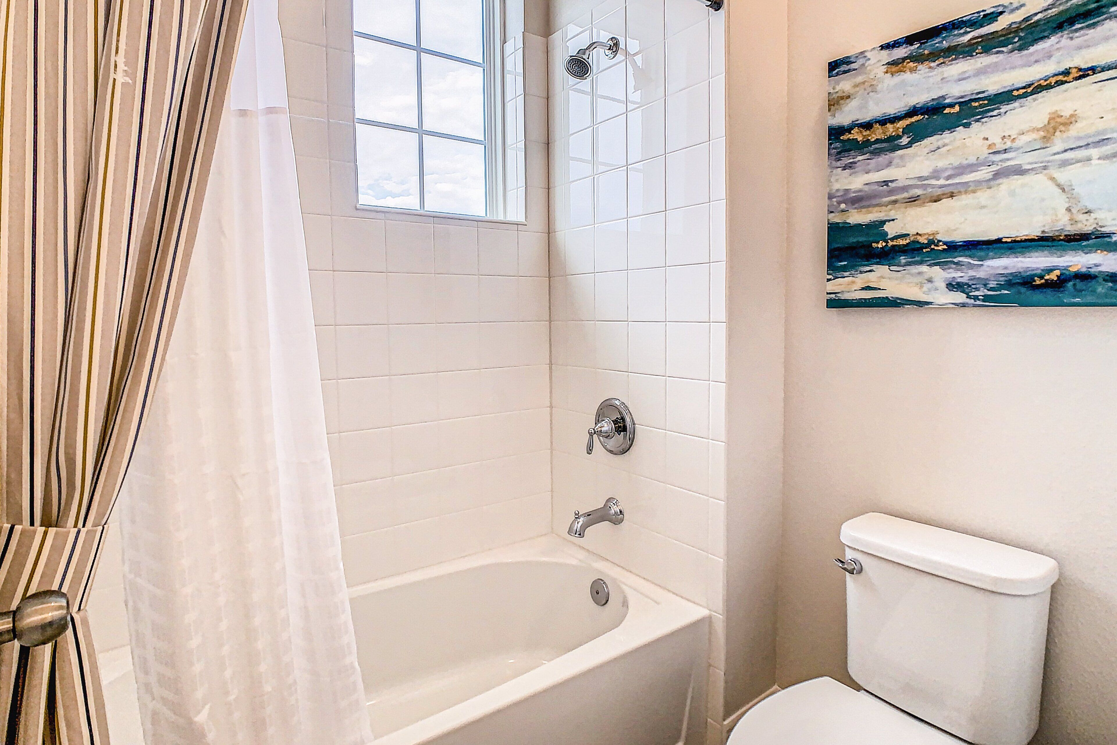 A bathroom with a bathtub, toilet, and a window.