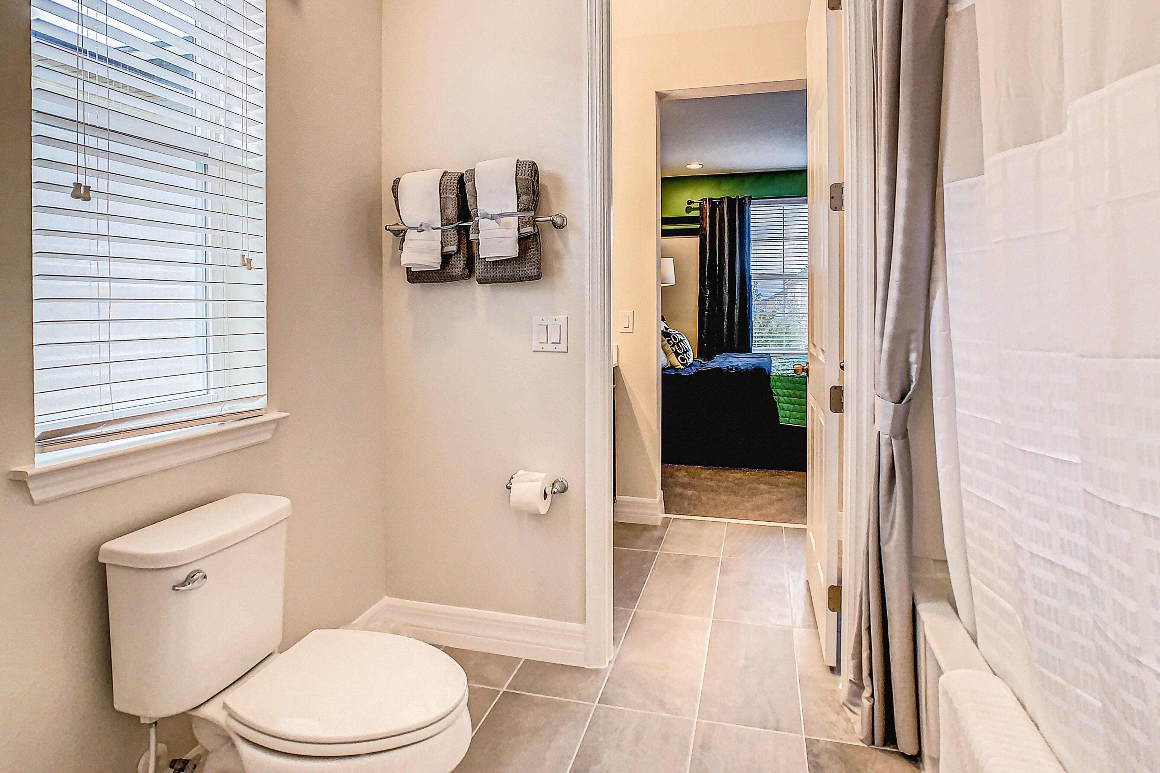A bathroom with a toilet, towel rack, and a window with blinds.