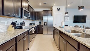 A modern kitchen with dark wood cabinets, stainless steel appliances, a granite countertop, and a built-in oven. - Luxury Home With Themed Bedrooms,arcade Games and Private Pool (Clermont)