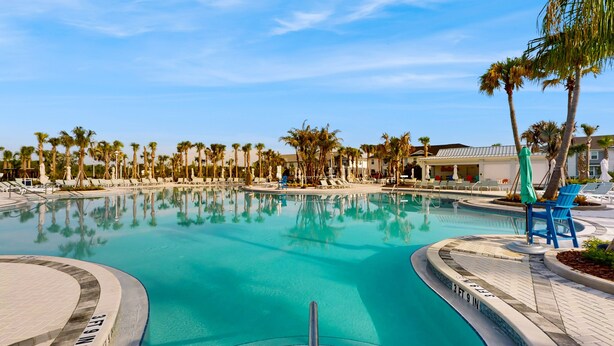 A swimming pool with clear blue water, surrounded by palm trees and lounge chairs. - Luxury Home With Themed Bedrooms,arcade Games and Private Pool (Clermont)