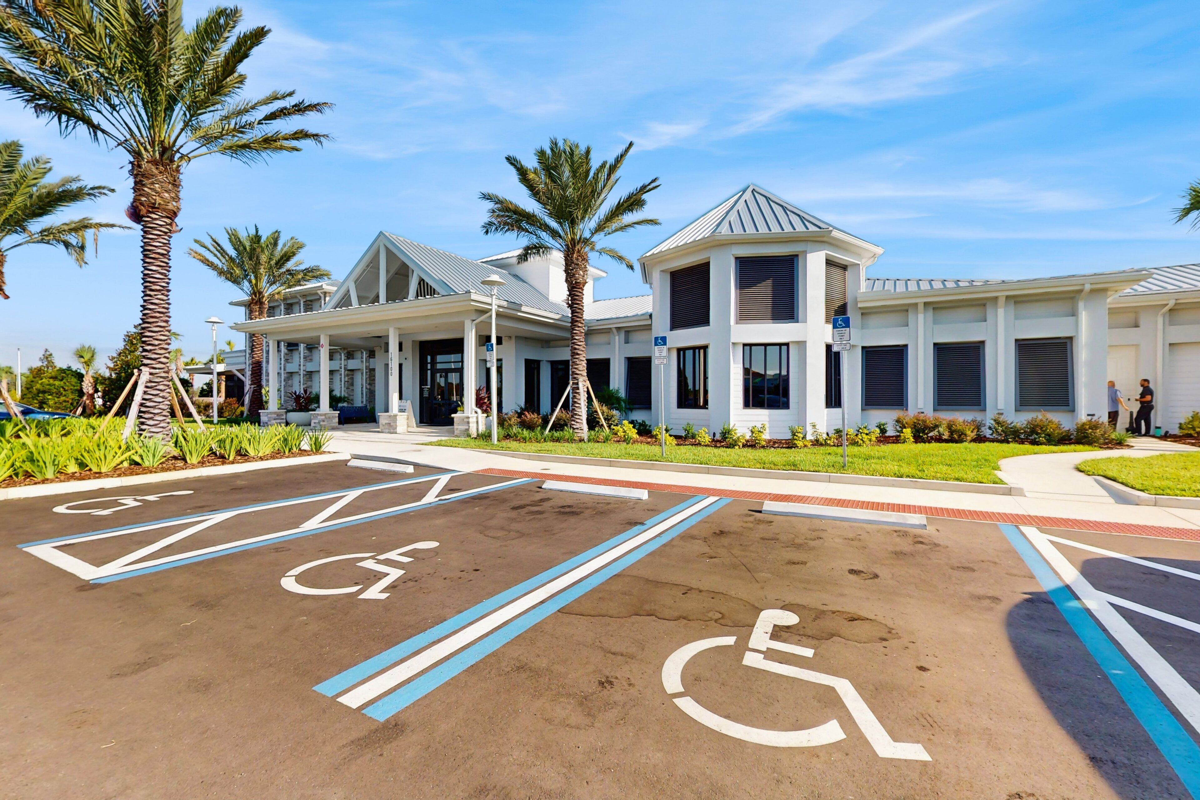 A parking lot with handicapped spaces, palm trees, and a building with a modern design.