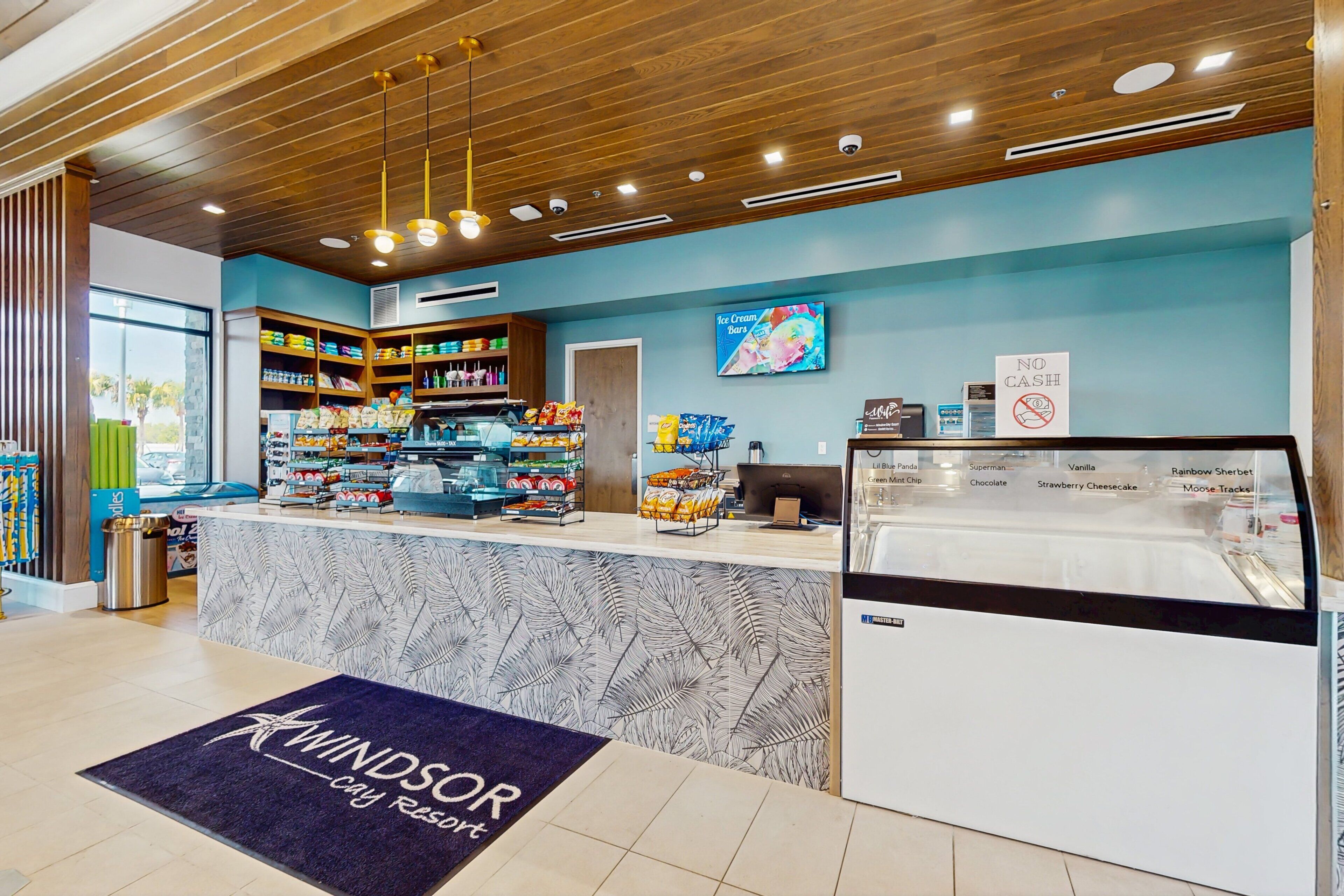 A hotel reception area with a counter, shelves stocked with snacks, a no cash sign, and a menu board.