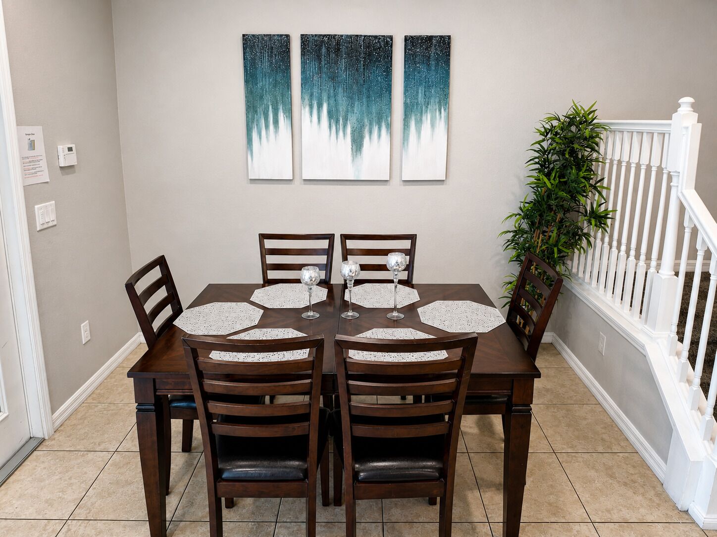 A dining room with a rectangular table, four chairs, and three wall-mounted paintings.