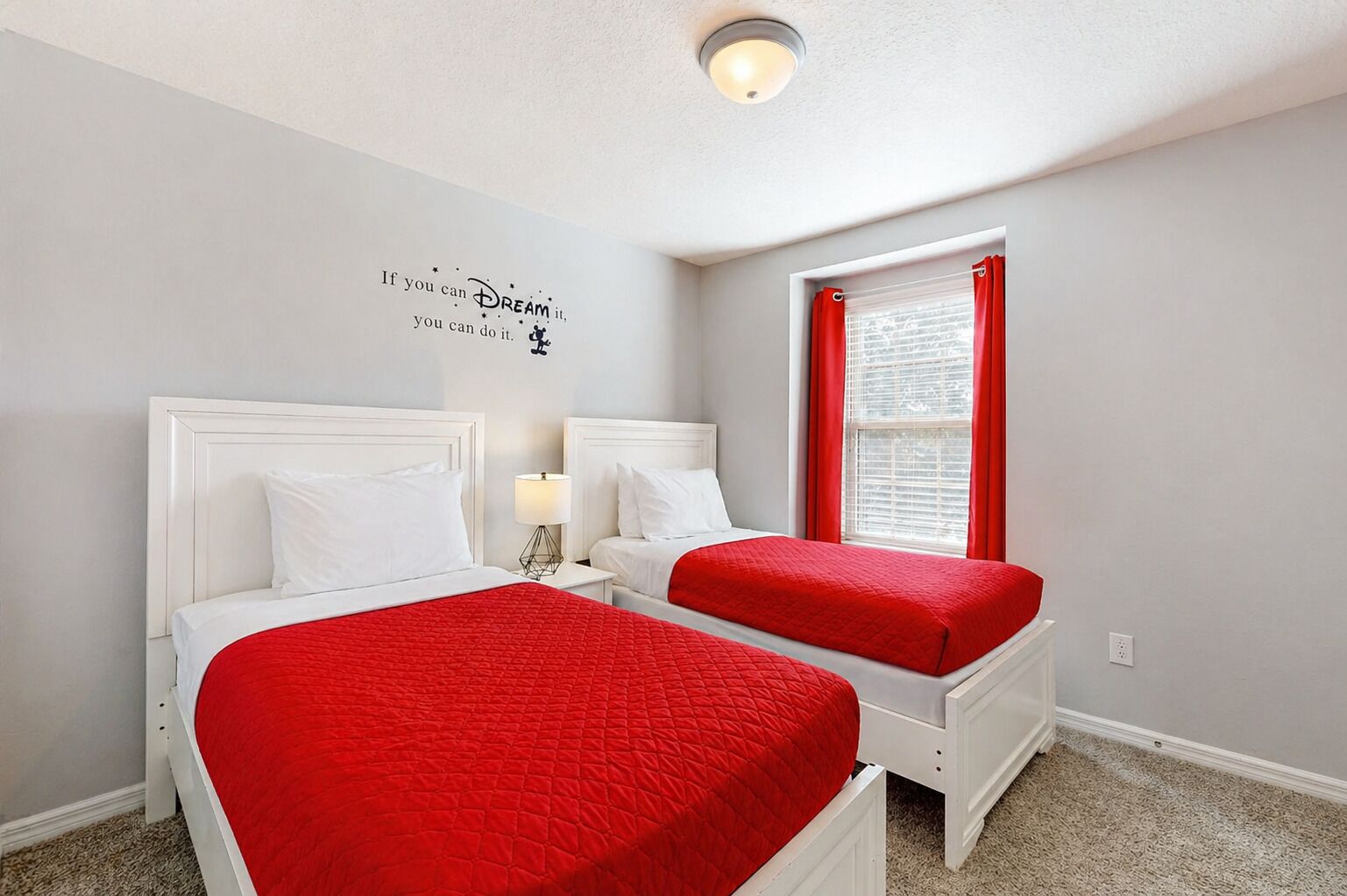 A bedroom with two beds, a window with red curtains, a wall decal, and a ceiling light.